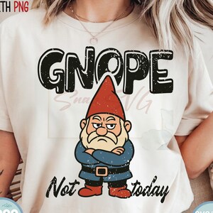May include: Cream-colored t-shirt featuring a grumpy garden gnome with the word "GNOPE" above it. Below the gnome, the text reads "Not today." The gnome wears a red hat, blue jacket, and black belt. The shirt has a distressed design.