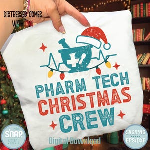 May include: White t-shirt with a pharmacy-themed Christmas design. The design includes a mortar and pestle, a Santa hat, and the words "PHARM TECH CHRISTMAS CREW" in teal and red. The shirt also has a string of lights and star accents.