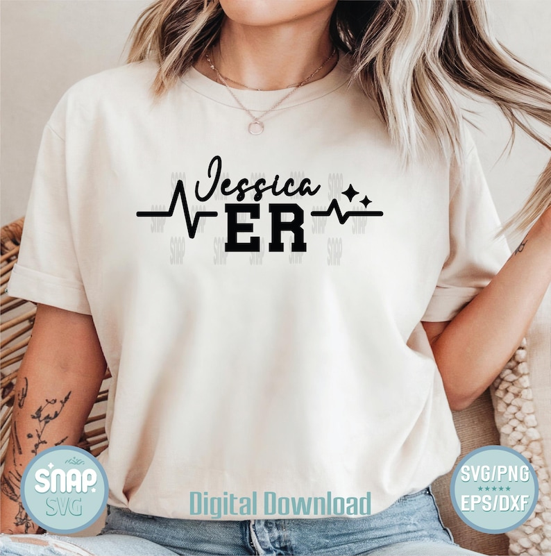 K&ouml;nnte beinhalten: Ein wei&szlig;es T-Shirt mit einem schwarzen Grafikdesign, auf dem "Jessica ER" mit einer Herzschlaglinie und zwei Sternen steht. Die Grafik ist mittig auf dem Shirt platziert.