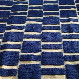 Blue and white Moroccan hand-knotted wool rug with a geometric grid of blue blocks on white, placed on tiled floor.