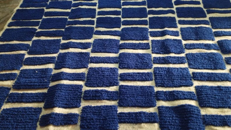 Blue and white Moroccan hand-knotted wool rug with a geometric grid of blue blocks on white, placed on tiled floor.