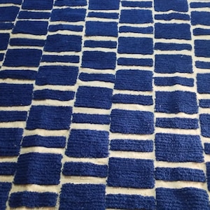 Blue and white Moroccan hand-knotted wool rug with a geometric grid of blue blocks on white, placed on tiled floor.