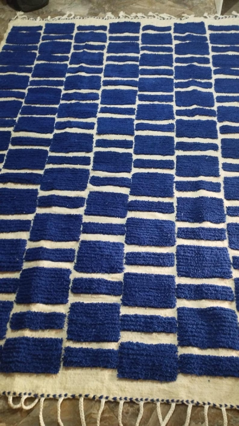 Blue and white Moroccan hand-knotted wool rug with a geometric grid of blue blocks on white, placed on tiled floor.