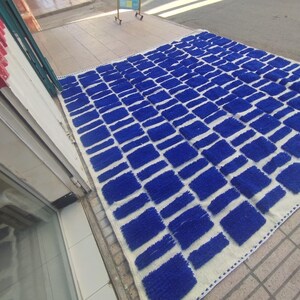 Blue and white Moroccan hand-knotted wool rug with a geometric grid of blue blocks on white, placed on tiled floor.
