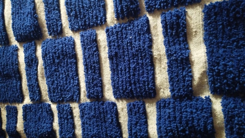 Blue and white Moroccan hand-knotted wool rug with a geometric grid of blue blocks on white, placed on tiled floor.