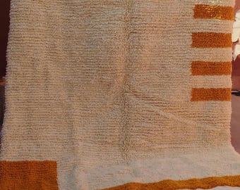 May include: A white and mustard yellow rug with a geometric pattern. The rug has a fringe border.