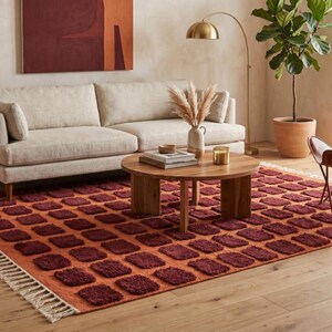 Dark red-orange checkered handwoven wool rug with white tassel fringe; boho modern tassel-edge rug for a reading nook.