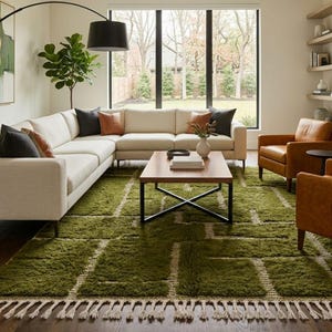 May include: A rectangular area rug featuring a deep olive green shag texture with a geometric grid pattern in cream white. The rug is finished with long, cream-coloured fringe tassels along the shorter edges, creating a textured floor covering.