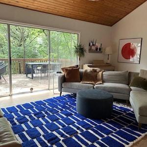 Blue and white Moroccan hand-knotted wool rug with a geometric grid of blue blocks on white, placed on tiled floor.