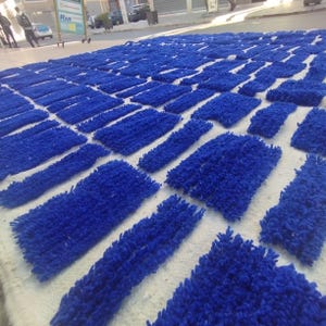 Blue and white Moroccan hand-knotted wool rug with a geometric grid of blue blocks on white, placed on tiled floor.