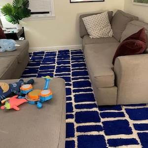 Blue and white Moroccan hand-knotted wool rug with a geometric grid of blue blocks on white, placed on tiled floor.