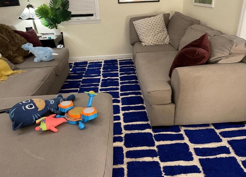 Blue and white Moroccan hand-knotted wool rug with a geometric grid of blue blocks on white, placed on tiled floor.