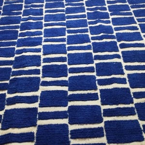 Blue and white Moroccan hand-knotted wool rug with a geometric grid of blue blocks on white, placed on tiled floor.