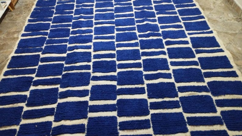 Blue and white Moroccan hand-knotted wool rug with a geometric grid of blue blocks on white, placed on tiled floor.