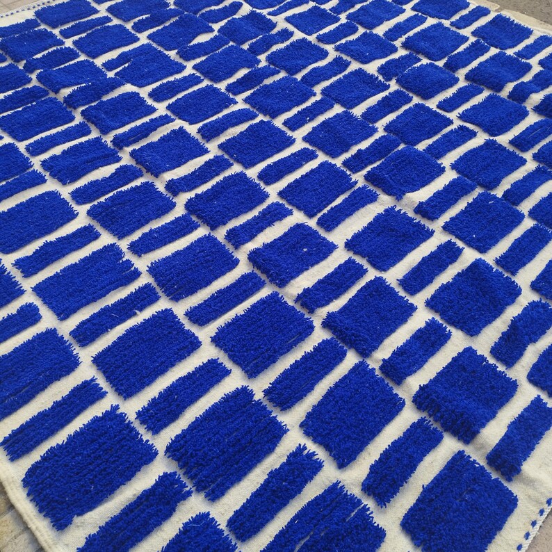 Blue and white Moroccan hand-knotted wool rug with a geometric grid of blue blocks on white, placed on tiled floor.