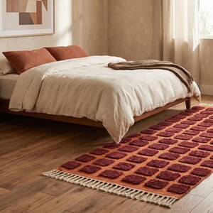 Dark red-orange checkered handwoven wool rug with white tassel fringe; boho modern tassel-edge rug for a reading nook.