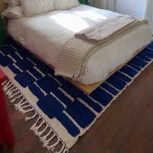 Blue and white Moroccan hand-knotted wool rug with a geometric grid of blue blocks on white, placed on tiled floor.
