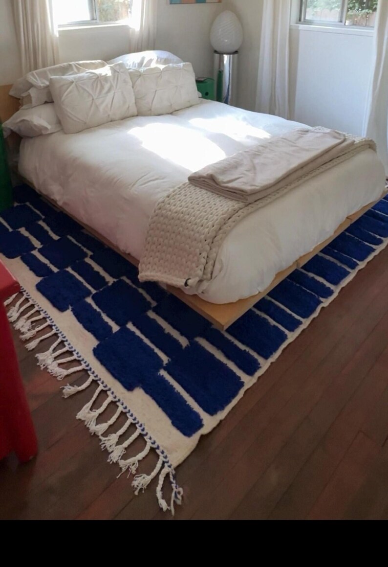 Blue and white Moroccan hand-knotted wool rug with a geometric grid of blue blocks on white, placed on tiled floor.