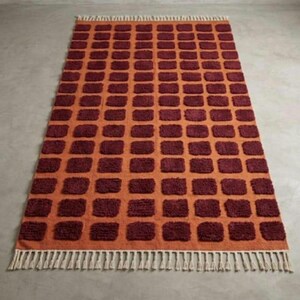 Dark red-orange checkered handwoven wool rug with white tassel fringe; boho modern tassel-edge rug for a reading nook.