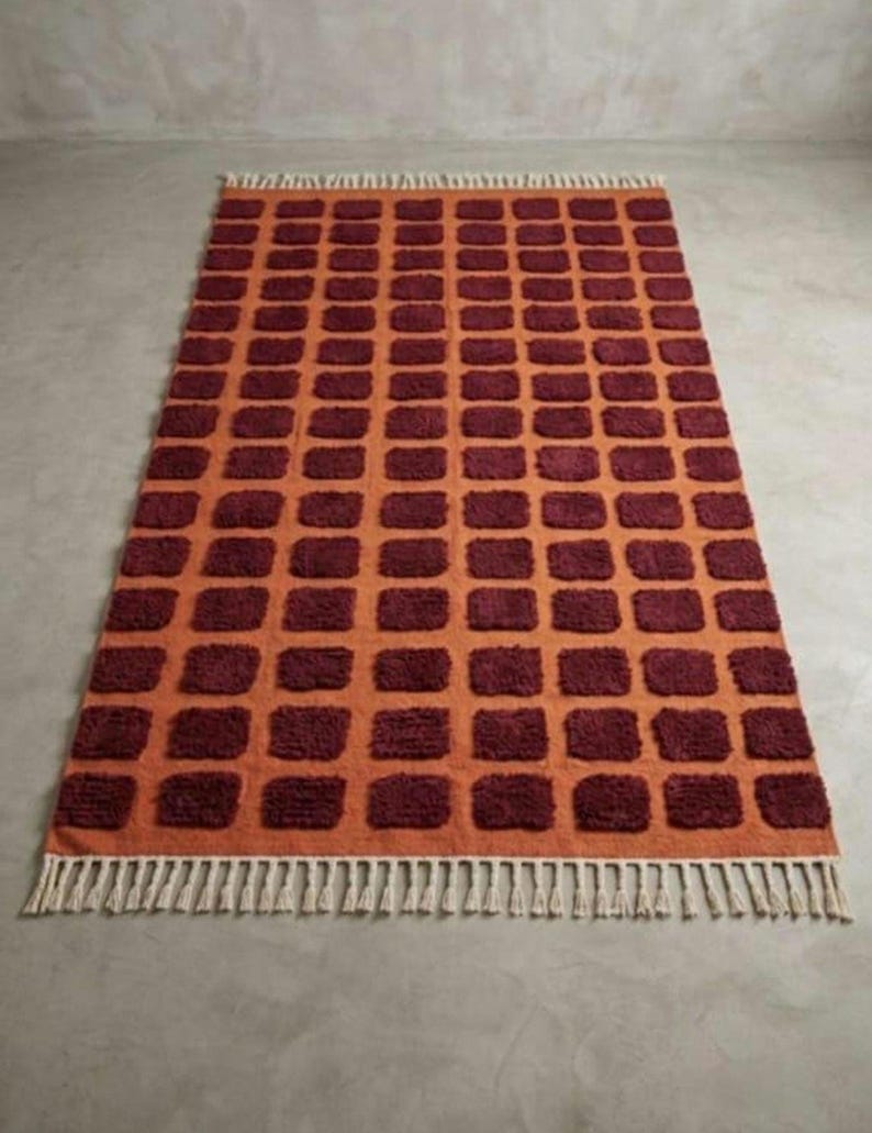 Dark red-orange checkered handwoven wool rug with white tassel fringe; boho modern tassel-edge rug for a reading nook.
