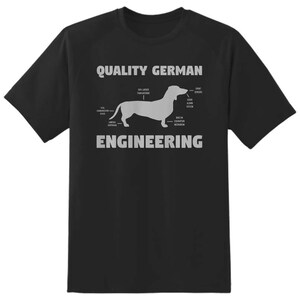 May include: Black t-shirt featuring a dachshund diagram with the text "QUALITY GERMAN ENGINEERING" in white. The diagram labels parts of the dog, including "50% Larger Than Average" and "Built-in Excavation Mechanism."