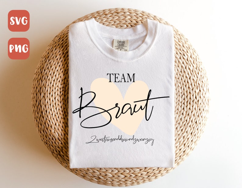 May include: White t-shirt with the text "TEAM Braut" in black lettering with a peach heart. The text "zweittausendundzwanzig" is written in black below the heart.