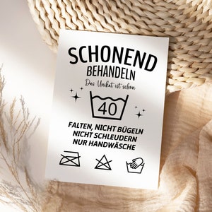 May include: A white card with black text and symbols. The text reads "Schonend Behandeln Das Unikat ist schon 40+ Falten, Nicht B&uuml;geln Nicht Schleudern Nur Handw&auml;sche". The card has symbols for hand washing, no ironing, no bleaching, and no tumble drying.