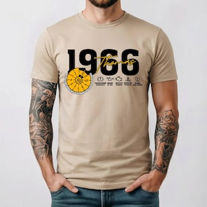 Könnte beinhalten: Ein beiges T-Shirt mit kurzen Ärmeln, das den schwarzen Text 1966, den gelben Schriftzug Thomas und eine gelbe kreisförmige Tacho-Grafik mit der Zahl 60 zeigt. Darunter befinden sich fünf schwarze Auto-Warnleuchten-Symbole mit deutschem Text.