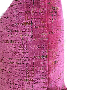 May include: A close-up of a pink decorative pillow with a textured, woven fabric. The pillow has a grid-like pattern with subtle variations in color, including hints of green and brown. The pillow is a vibrant accent piece.