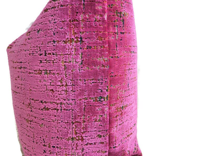 May include: A close-up of a pink decorative pillow with a textured, woven fabric. The pillow has a grid-like pattern with subtle variations in color, including hints of green and brown. The pillow is a vibrant accent piece.
