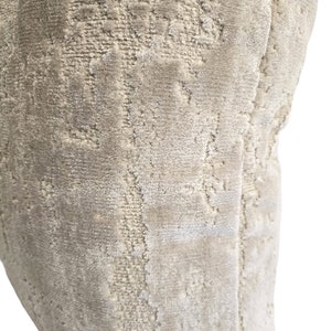 May include: A close-up of a beige velvet pillow with a subtle embossed pattern. The pillow is soft and plush, with a luxurious feel.