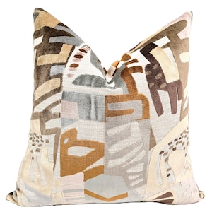 May include: A decorative throw pillow with a geometric pattern in shades of brown, beige, gray, and pink. The pillow features abstract shapes and lines, creating a modern and stylish design.
