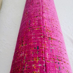May include: A rolled-up, vibrant fuchsia-colored fabric with a textured, woven appearance. The fabric has a subtle pattern with flecks of yellow, blue, and green. The item appears to be a decorative textile, possibly for upholstery or home decor.