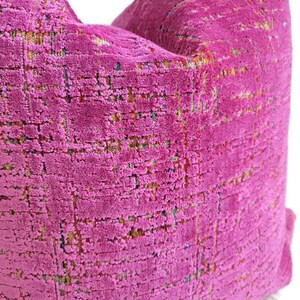 May include: Close-up of a vibrant fuchsia pillow with a textured, woven appearance. The fabric has a grid-like pattern with subtle flecks of yellow, green, and blue, creating a rich, multi-tonal effect. The pillow is a decorative home accent.