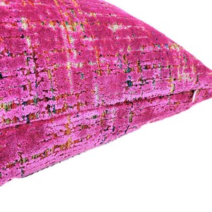 May include: Close-up of a fuchsia-colored decorative pillow. The pillow has a textured, woven appearance with a grid-like pattern. The fabric has a plush, velvety feel, and the color is vibrant and eye-catching.