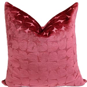 May include: A red velvet pillow with a geometric pattern. The pillow is made of a soft, plush fabric and has a subtle sheen.