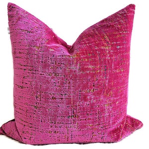 May include: A vibrant fuchsia decorative pillow with a textured, woven appearance. The pillow features a grid-like pattern with subtle flecks of gold, green, and blue. The pillow is square and has a soft, plush look, perfect for adding a pop of color to any room.