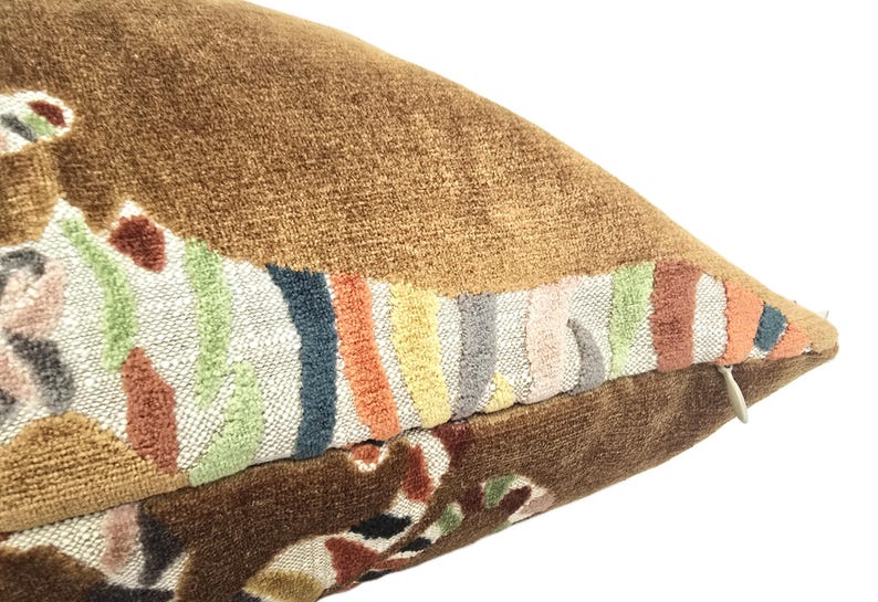Peut inclure: Un coussin en velours marron avec un motif brod&eacute; color&eacute;. Le motif pr&eacute;sente une s&eacute;rie de rayures et de formes abstraites dans des tons de rose, orange, jaune, vert, bleu et gris.
