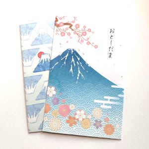 May include: Two Japanese-style envelopes. One features a repeating pattern of blue mountains with a red sun. The other has a blue mountain with a cherry blossom branch and the Japanese text "Otoshidama". Floral and wave patterns decorate the bottom.