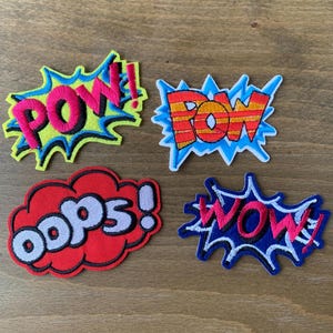 May include: Four colorful embroidered iron-on patches with comic book style speech bubbles. The patches say "POW!" "POW!" "OOPS!" and "WOW!"