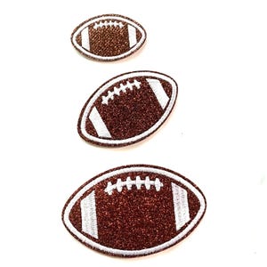 May include: Three oval-shaped football patches arranged vertically in descending size. Each patch features a brown glittery surface with white embroidered stitching details and white stripes at both ends, creating a textured appearance.