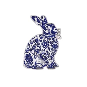 May include: A blue and white decorative rabbit figurine. The rabbit is in a seated position with its ears perked up. The rabbit's body is decorated with a floral pattern. The figurine has a bow tie and gray feet.