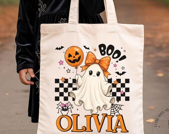 May include: A cream-colored canvas tote bag featuring a graphic print of a white ghost with an orange bow, an orange jack-o'-lantern balloon, a black and white checkered pattern, a spider, and the text "BOO!" and the name "OLIVIA" in orange.