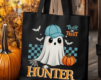 May include: A black tote bag featuring a graphic of a white ghost wearing a blue baseball cap, holding a small orange pumpkin. The design includes a teal checkered pattern, white bats, a spider web, and the text Trick or Treat and Hunter.