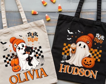 May include: Two canvas tote bags, one cream and one black, each featuring a ghost wearing an orange beanie, a pumpkin, and a checkered pattern. The cream bag displays the name Olivia, and the black bag displays the name Hudson, both with Trick or Treat text.