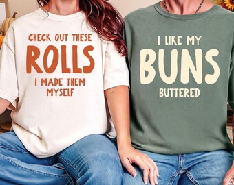 May include: A cream-colored t-shirt with the text "CHECK OUT THESE ROLLS I MADE THEM MYSELF" in brown and a sage green t-shirt with the text "I LIKE MY BUNS BUTTERED" in cream. A matching beverage cooler features "THANKSGIVING 2024 THE MILLERS CHEERS!"
