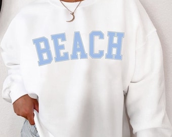 May include: White sweatshirt with a light blue "BEACH" graphic in a collegiate font.