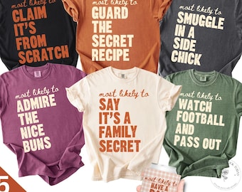 May include: Six short-sleeved t-shirts in black, orange, charcoal, maroon, cream, and olive green, each featuring the text 'most likely to' followed by phrases like 'CLAIM IT'S FROM SCRATCH', 'GUARD THE SECRET RECIPE', 'SMUGGLE IN A SIDE CHICK', 'ADMIRE THE NICE BUNS', 'SAY IT'S A FAMILY SECRET', 'WATCH FOOTBALL AND PASS OUT', and a can cooler reading 'MOST LIKELY TO HAVE A DAM GOOD TIME'.