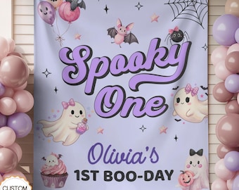 May include: A light purple rectangular backdrop featuring the text Spooky One, Olivia's 1ST BOO-DAY, and illustrations of ghosts, a bat, a spider, a cupcake, balloons, and a spiderweb. The design includes stars and sparkles in a pastel color palette.