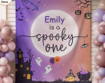 May include: A rectangular fabric backdrop featuring a purple and orange gradient background with a large white moon. The text reads "Emily is a spooky one". Graphics include a black haunted house, ghosts, bats, pumpkins, and a cauldron.